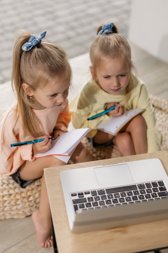our-experience Two young girls focus on online lessons, writing in notebooks during a virtual class.
